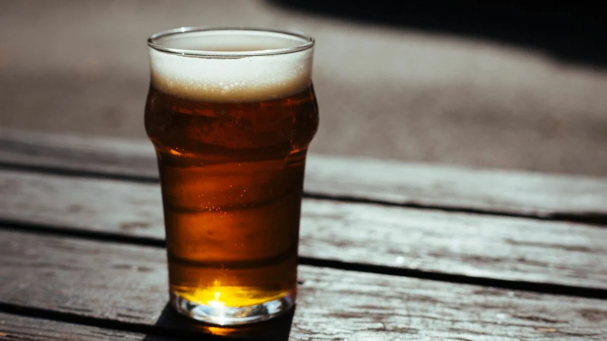 Verre de bière dorée posé sur une table en bois au soleil, dans l'esprit de la 3 Monts IPA